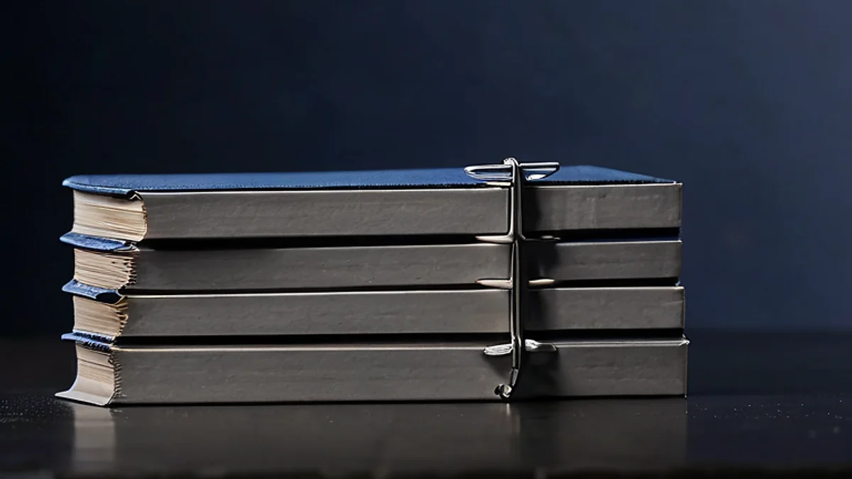 A stack of bound grey files held together by a steel clip on a dark desk.