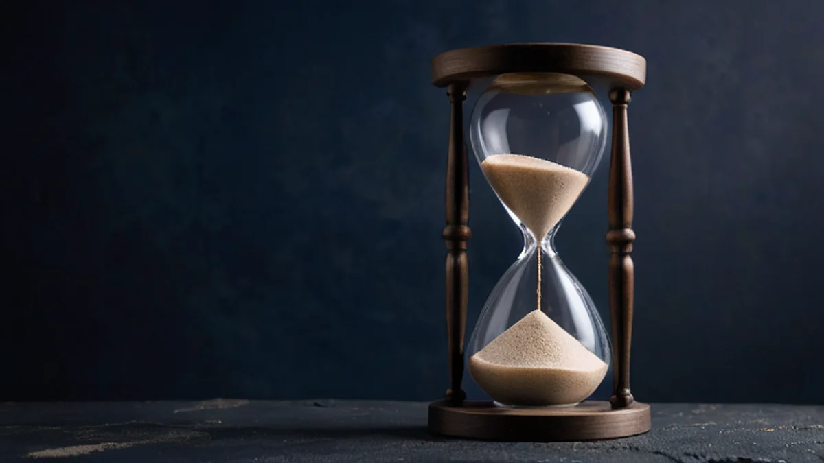Un reloj de arena con arena clara sobre piedra oscura, bajo una luz fría.