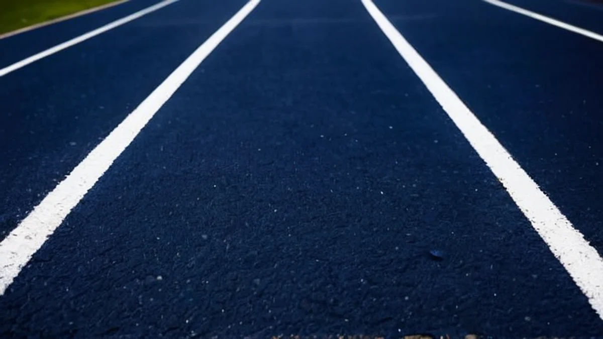 White lane lines on a dark blue running track, seen from a low angle in evening light.