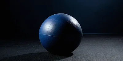 Un balón de ejercicio azul marino y liso sobre un suelo de gimnasio de caucho oscuro, bajo una sola luz cenital.