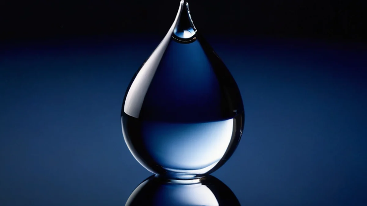 A single drop of clear water on a dark blue glass surface, seen close up.
