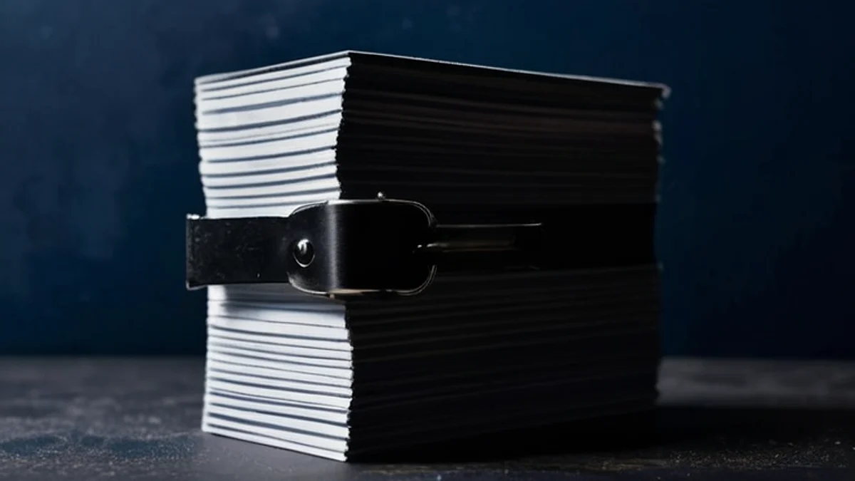 A thick stack of blank cards held together by a black strap on a dark desk.