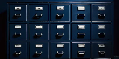 Filas de cajones de archivo azul marino idénticos, con portaetiquetas en blanco, bajo una luz fría.